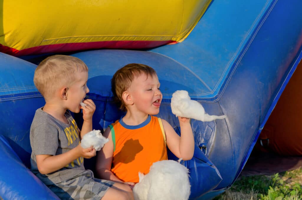 Zwei Freunde essen vor einer Hüpfburg Zuckerwatte